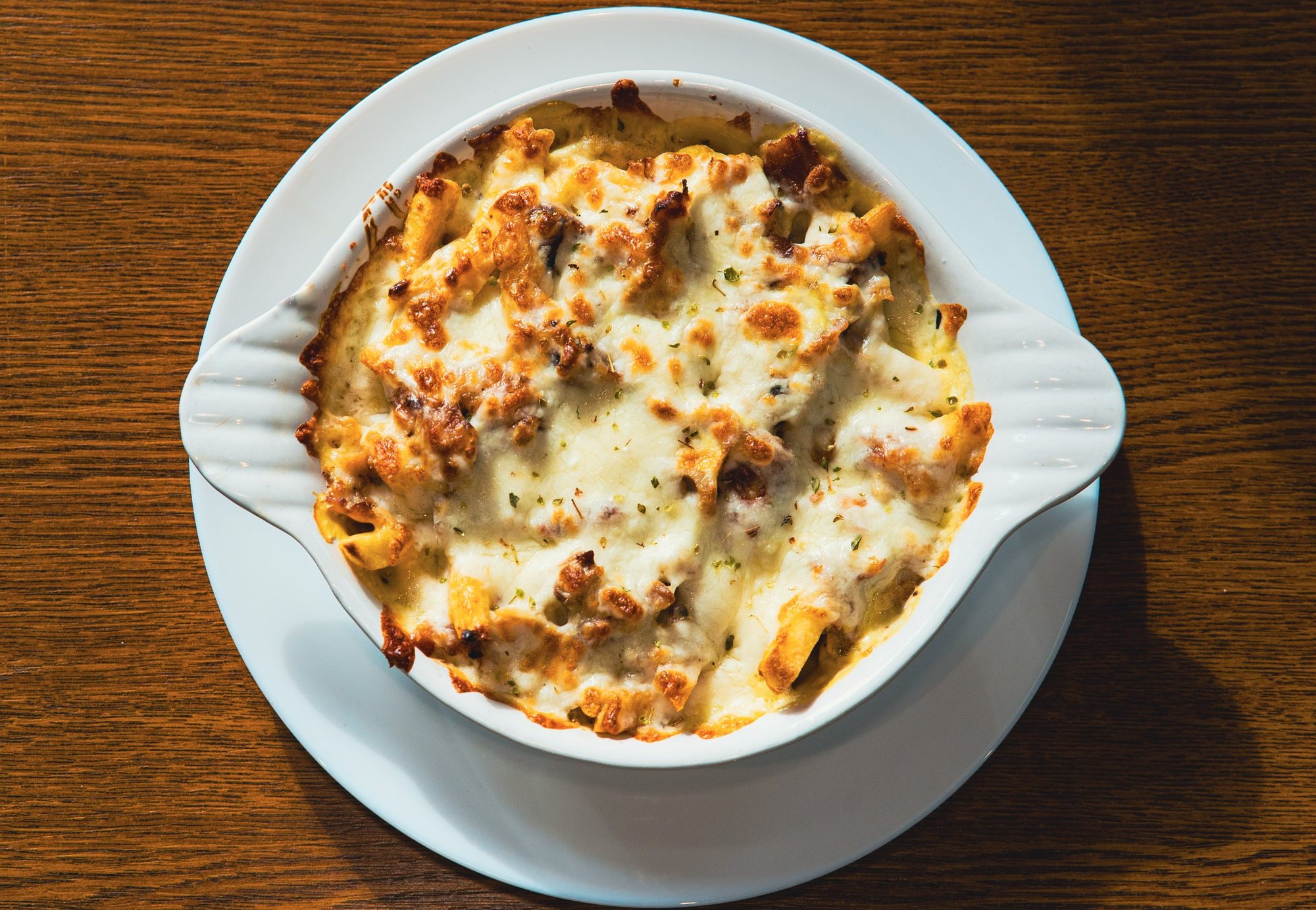 Photographe culinaire à Strasbourg : gratin de pâtes gratiné vu du dessus, assiette blanche sur table en bois