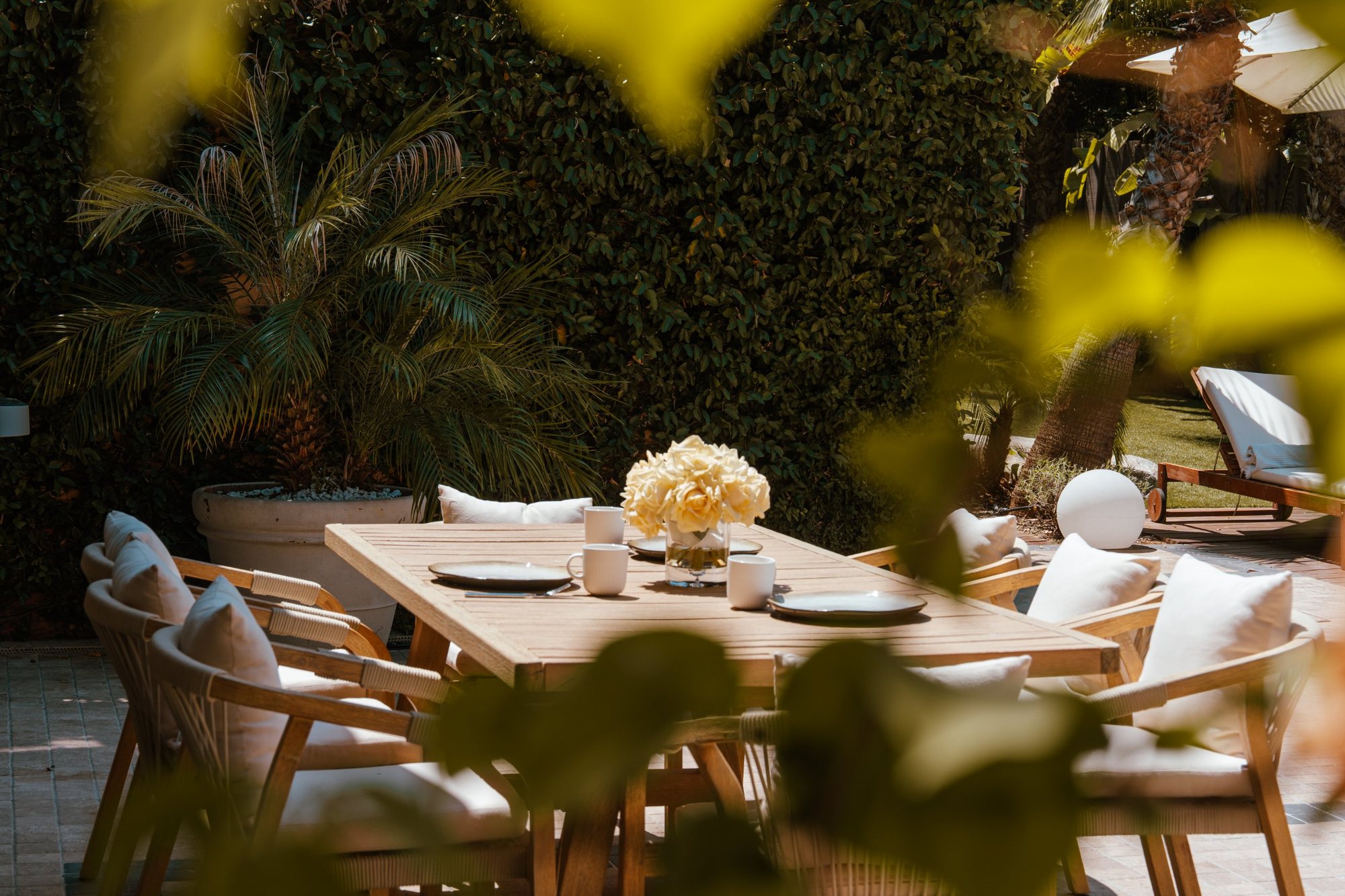 Photographe d’espaces extérieurs : table dressée au jardin, vue à travers le feuillage