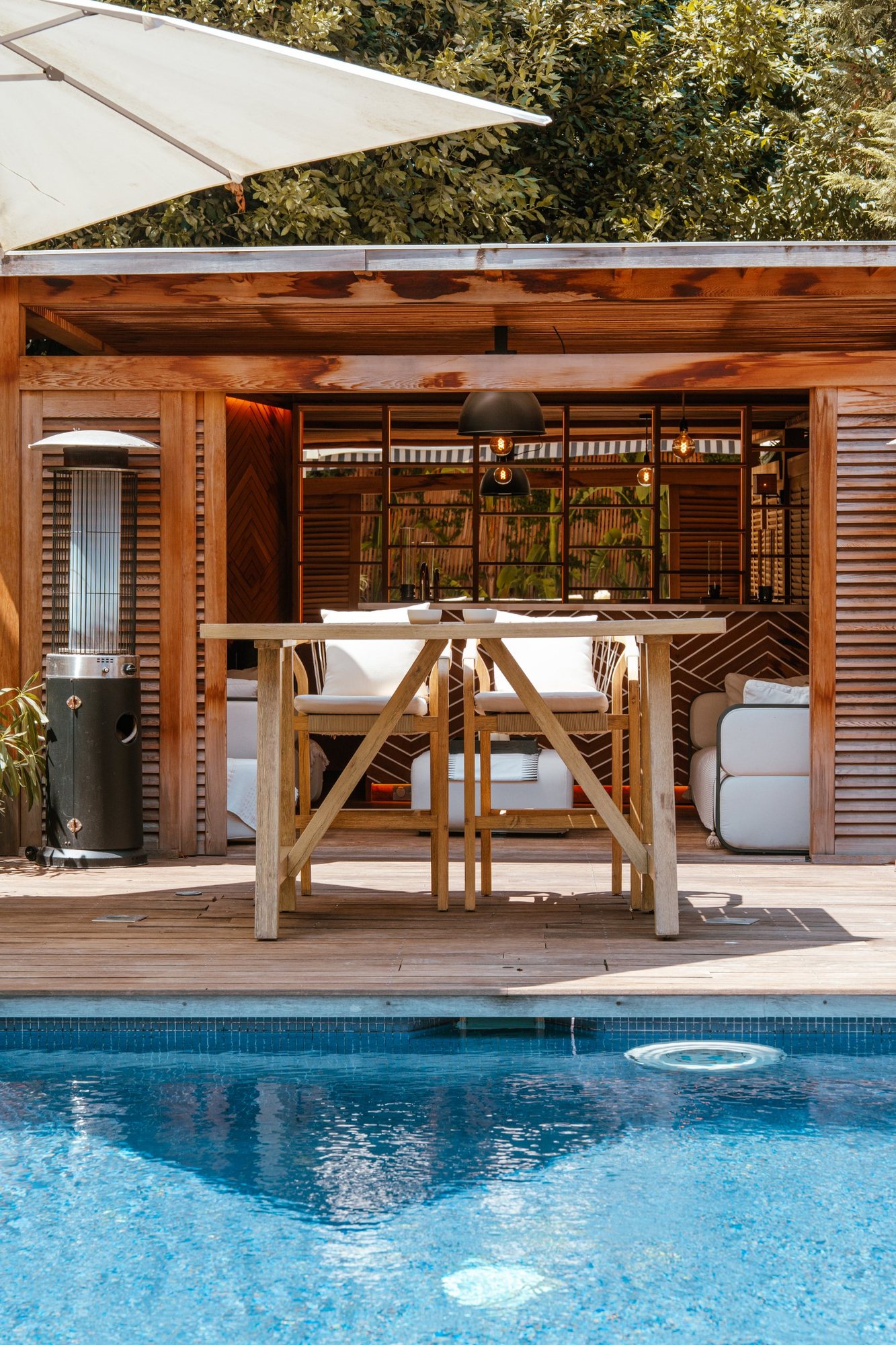 Photographe d’espaces extérieurs : pool house en bois avec bar et chaises face à la piscine