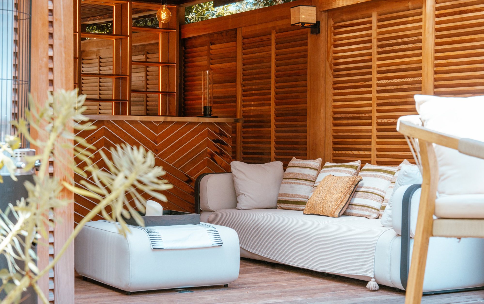 Photographe d’espaces extérieurs : salon d’un pool house en bois, canapé et coussins rayés