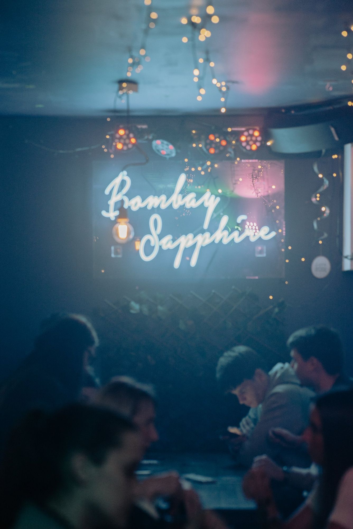Photographe événementiel à Strasbourg : néon Bombay Sapphire dans un bar, clients flous au premier plan
