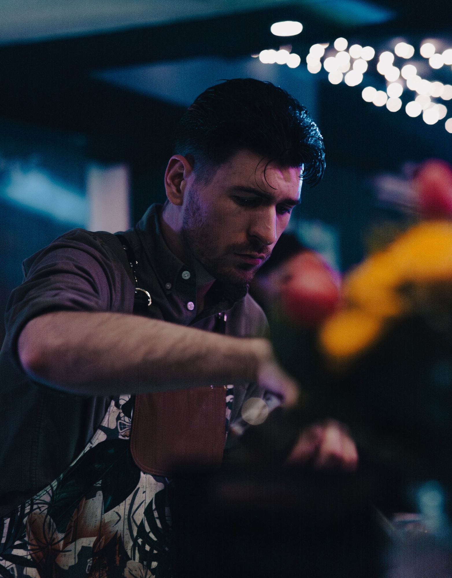 Photographe de bar à Strasbourg : barman concentré préparant un cocktail, lumières bokeh