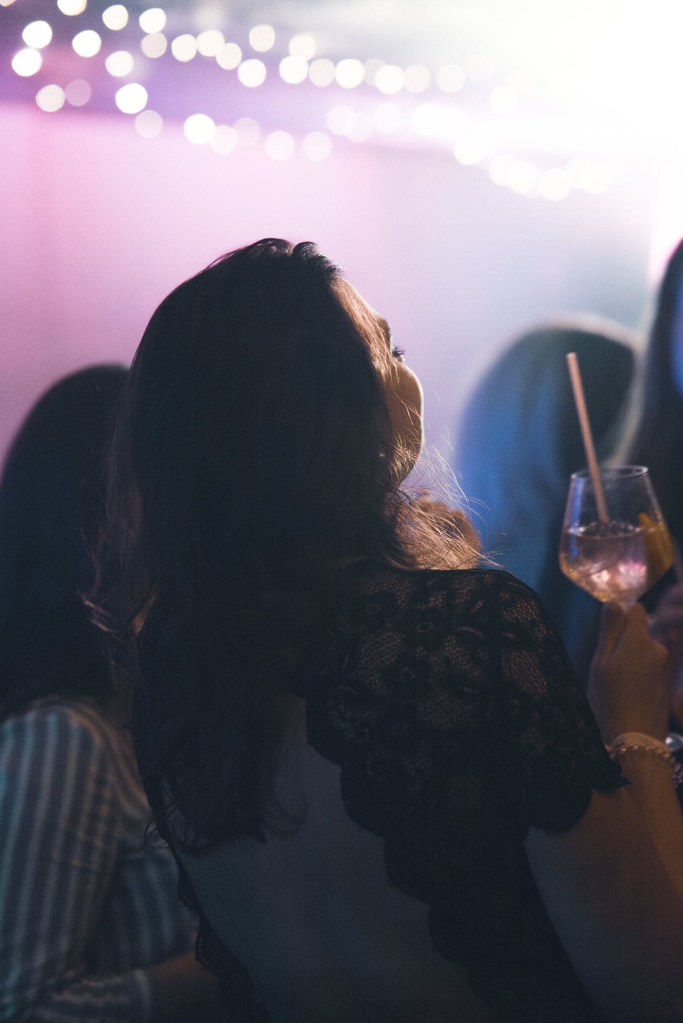 Photographe événementiel à Strasbourg : silhouette d’une invitée un verre à la main, guirlandes lumineuses et ambiance rose