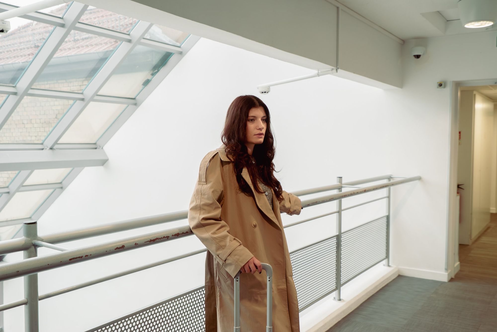 Photographe lifestyle à Strasbourg : femme en trench sur une passerelle vitrée de l’hôtel