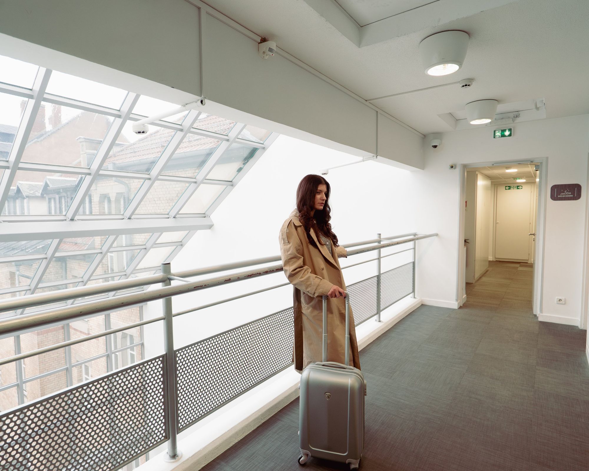 Photographe d’hôtel à Strasbourg : voyageuse en trench avec sa valise sur la passerelle vitrée