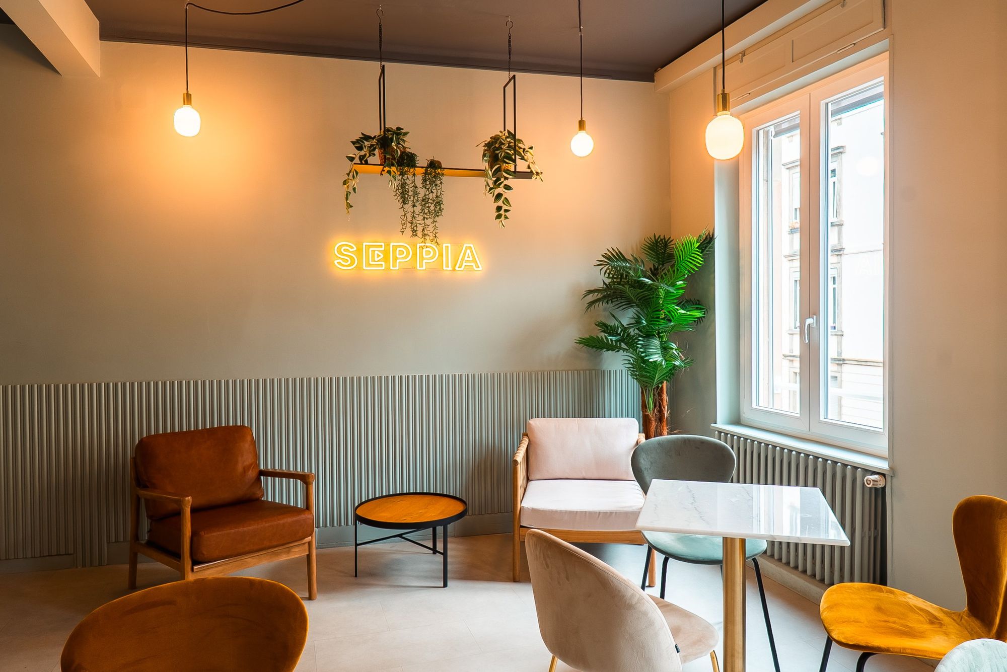 Photographe d’intérieur à Strasbourg : salon chaleureux avec néon Seppia, fauteuils, suspensions et grande fenêtre