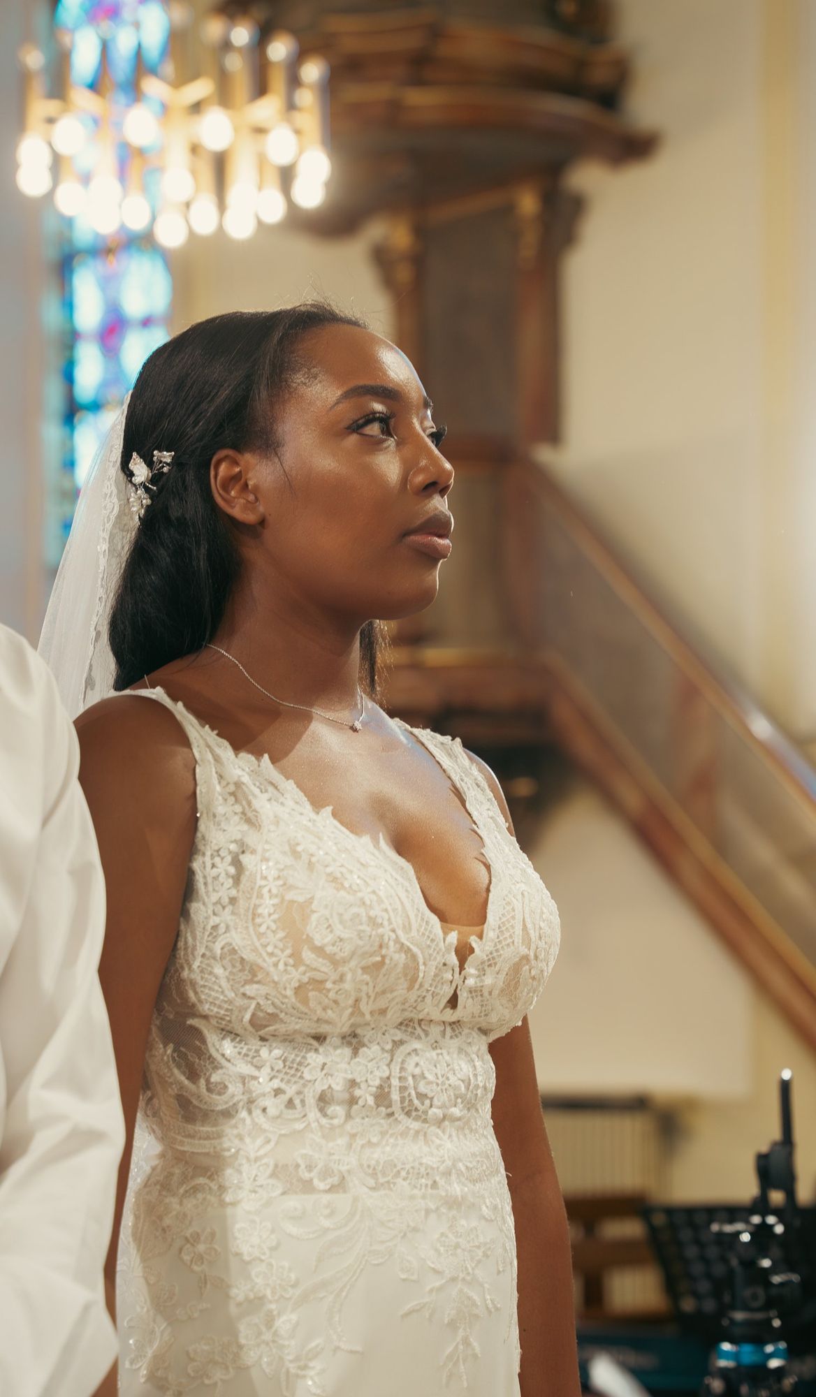 Photographe de mariage à Strasbourg : portrait de profil de la mariée pendant la cérémonie, vitrail et lustre en arrière-plan