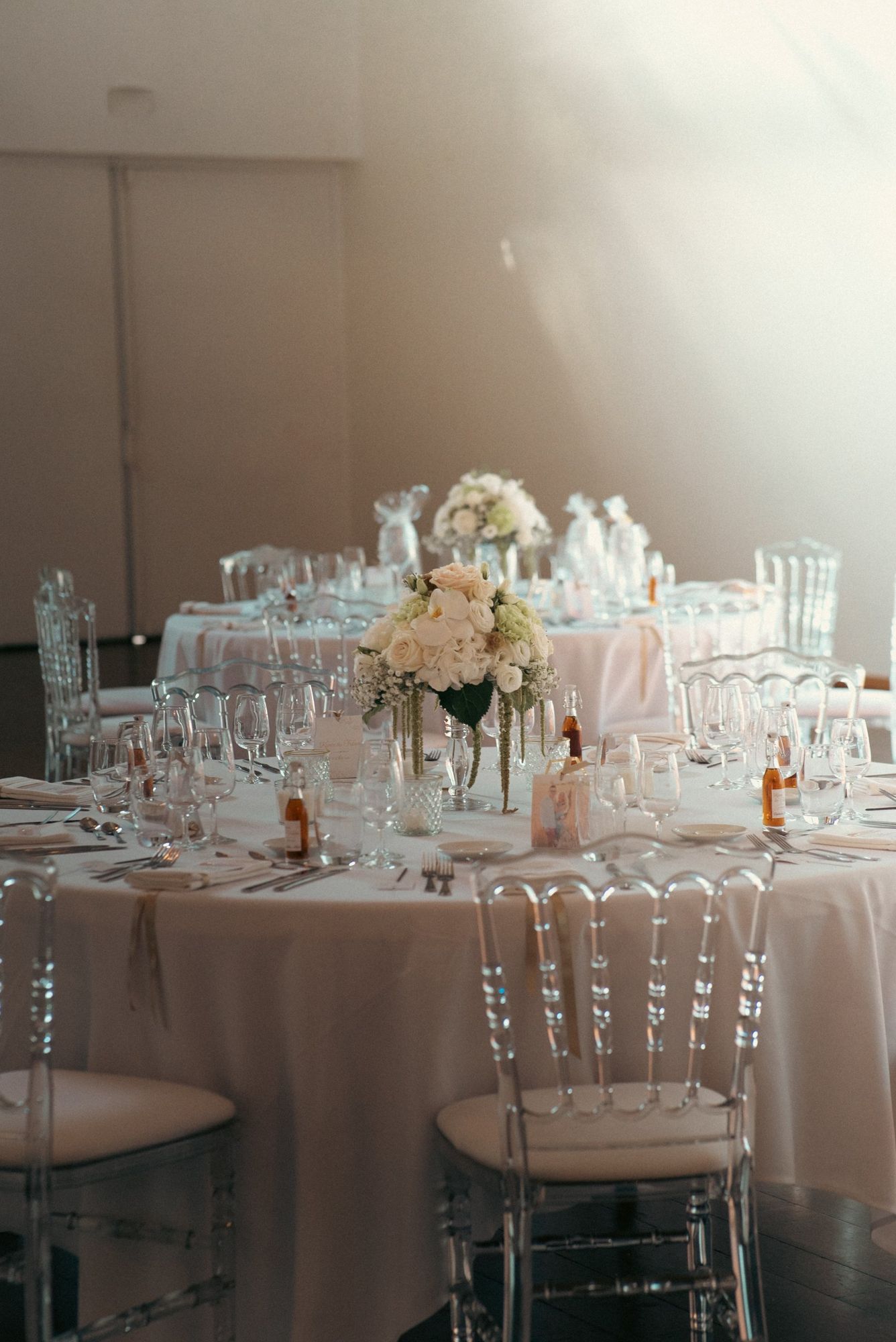 Photographe de mariage à Strasbourg : tables rondes de réception, chaises transparentes et bouquets blancs