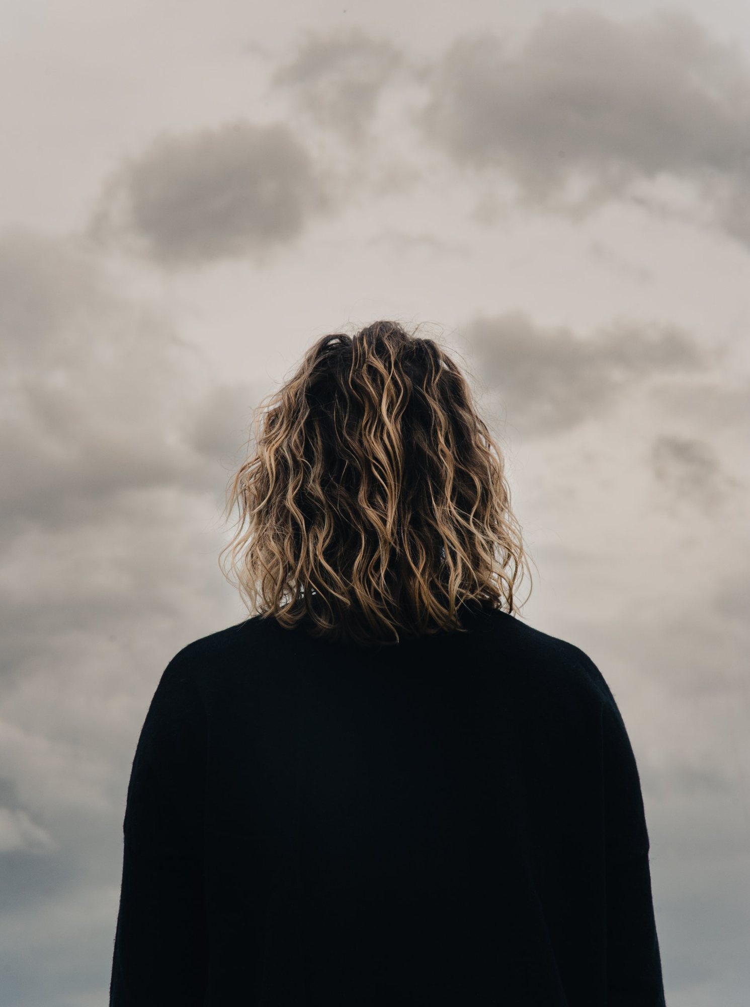 Shooting photo en extérieur : une femme de dos, cheveux bouclés, face aux nuages